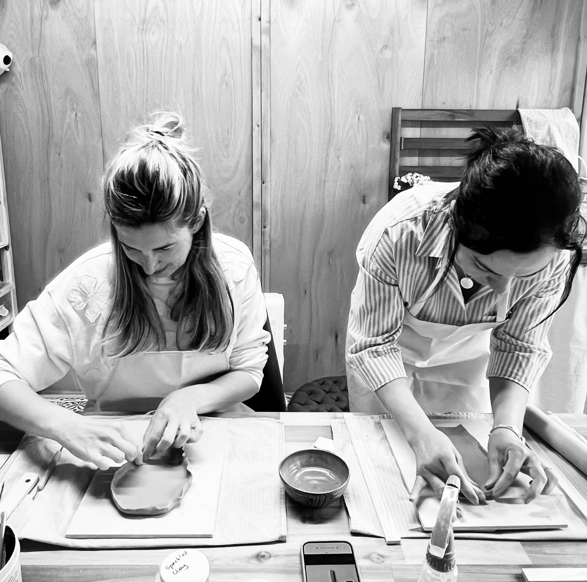 Two guests handbuilding clay pieces together at the studio table